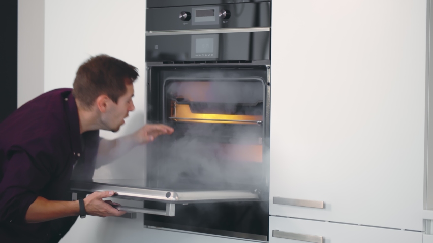 Young Shocked Man Opening Oven Filled With Smoke In Kitchen. Bad cook guy burning dinner in electric oven. Handsome male open built-in oven with burnt meal | Shutterstock HD Video #1063776691