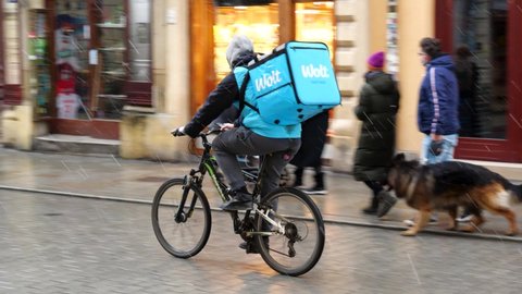 Krakow, Małopolska, Poland - November 2020: Wolt company bike driver, fast food delivery biker passing by, riding through the crowdy street. Mobile app online food ordering, food-delivery platform