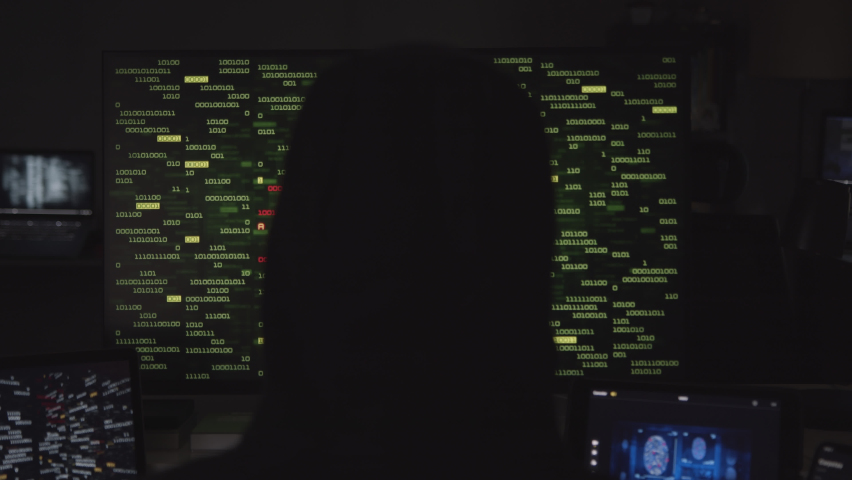 Hooded hacker working on computer. Dark room with devices playing several videos: internet security, program code security interface and fingerprint access. Technology. Cyber security.  Royalty-Free Stock Footage #1063777402