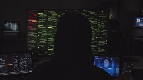 Hooded hacker working on computer. Dark room with devices playing several videos: internet security, program code security interface and fingerprint access. Technology. Cyber security. 