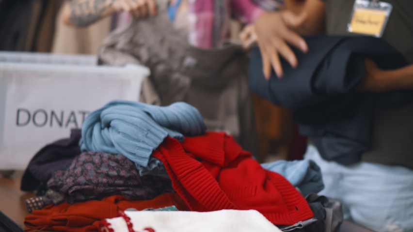 Close up of volunteers sorting donated clothes in charity shop. Team of workers unpacking boxes with clothes in second hand store. Charity and donation concept Royalty-Free Stock Footage #1063780618