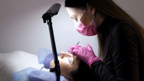 Face of a young girl before a modern eyelash lamination procedure in a professional beauty salon. The master applies special glue before the eyelash curling procedure in pink rubber gloves and a mask.