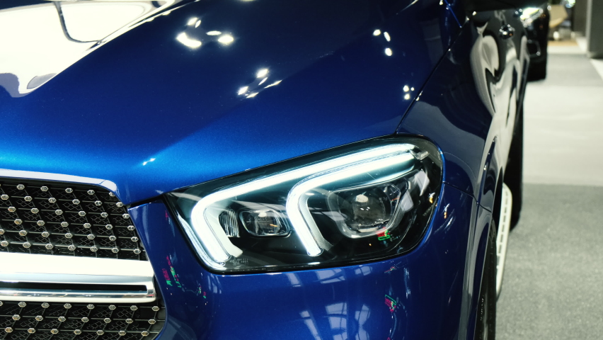 Turns on and off the dipped and main beam headlights. Close-up of the headlight of a new blue car in the showroom. Modern laser headlights. Led lights. Xenon. Bixenon.
