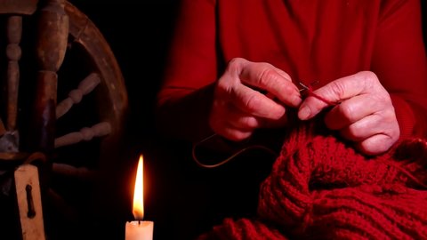 Hand knitting by candlelight in the dark. Knitting needles. Woolen thread. Hands of an old man. Handwork. Weave warm clothes. Manual creativity. Handmade. Flame of fire of a burning candle.