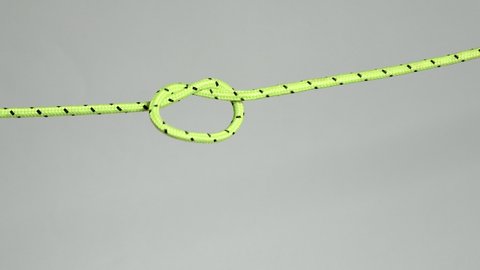 A simple knot is tightened on a green nylon cord on a light gray background