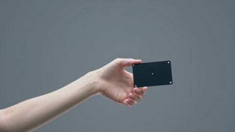 Woman's hand showing black plastic bank card with tracking points on gray studio background, advertising video