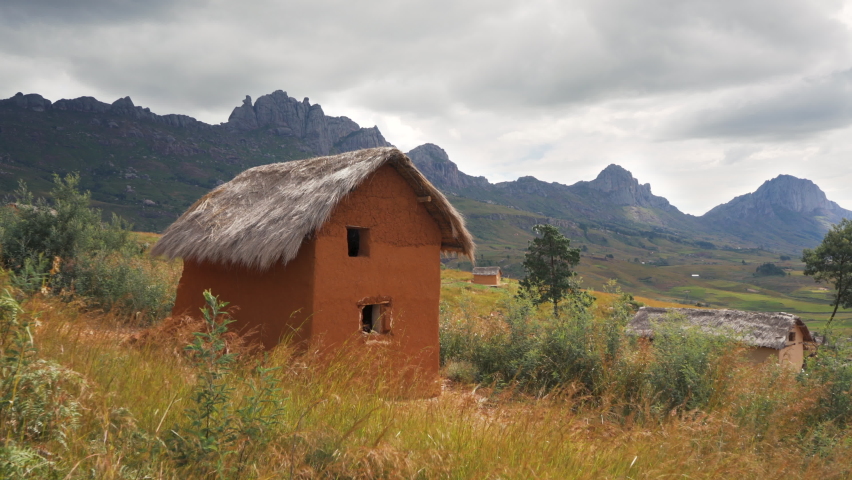 Typcial landscape at Andringitra National Park, Madagascar on sunny day. Rocky mountains with rice fields under at distance, small clay house with stray roof in foreground