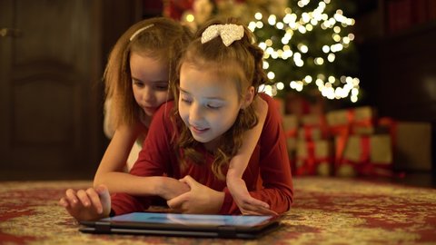 Two little girls write a letter to Santa Claus on a tablet