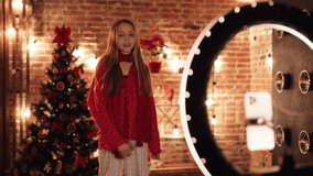 Portrait of cute Caucasian Girl, Kid, Child is recording New Video for Tik-Tok, New Vlog. Little blonde Blogger, Vlogger on Christmas Decoration. Winter Holidays. Easy Technology. Fests Indoor.