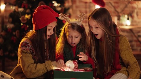 Three exited, Extremely Happy Sisters, Friends opening, unpacking their Christmas Gifts in the Cozy Evening. Big Family celebrating Winter Fests, opening Christmas Santas Presents. Festive Mood.