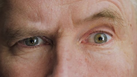 Face of surprised or doubtful elderly middle aged man raising eyebrow. Skeptical mature male senior citizen with wrinkles on attractive face looking at camera. Slow motion, macro extreme close up, 4K.