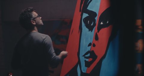 Adult man painting black outline while creating pop art portrait of woman in dark studio