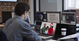 Caucasian man wearing face mask on video chat at christmas in office. christmas time festivity during covid 19 coronavirus pandemic.