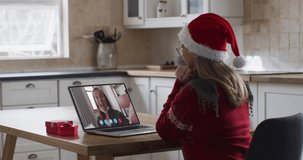 Caucasian woman wearing santa hat using laptop on video chat during christmas at home. communication with friends and family at christmas time during covid 19 coronavirus pandemic.