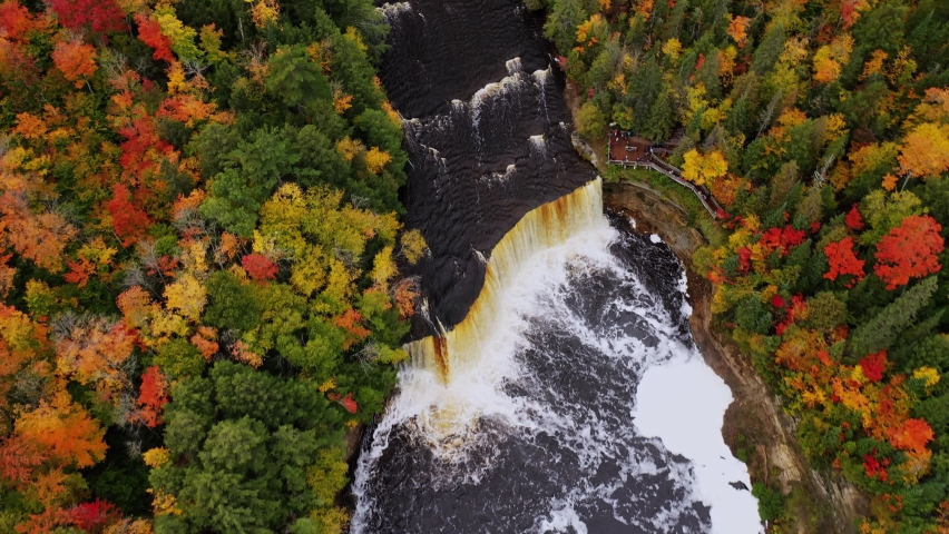 Beautiful aerial look down fly over of Tahquamenon falls waterfall cascade and the tourist viewing platform below surrounded by evergreen trees and fall or autumn colored foliage leaves.