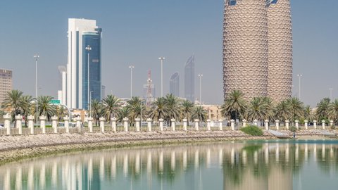 View of skyscrapers skyline with towers in Abu Dhabi timelapse. Reflections on water and palms on the street. United Arab Emirates