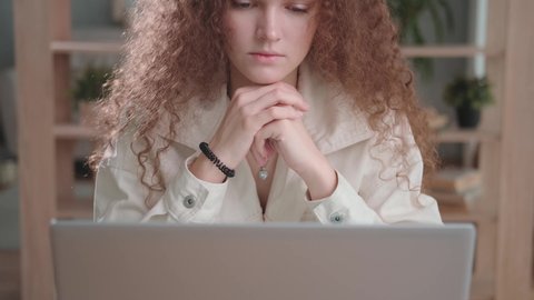 A concentrated tired young woman in a white suit sits at a table, thinks, looks to the side. Working day: a woman at work is preoccupied with problems. Portrait