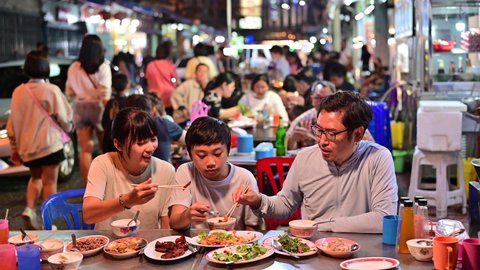 4K Asian family eating food on street food restaurant at Bangkok Chinatown with traffic