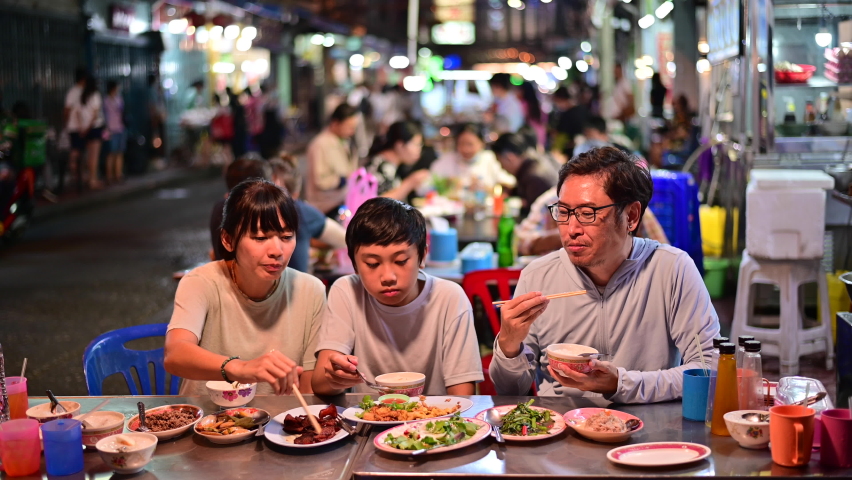4K Asian family enjoy eating food on street food restaurant with crowd of people at Yaowarat road, Bangkok Royalty-Free Stock Footage #1063817944