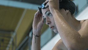 Woman athlete nervously take a deep breath, focus to start swimming, put her goggles on and prepare to jump to the pool. Slow motion video. Top shot.