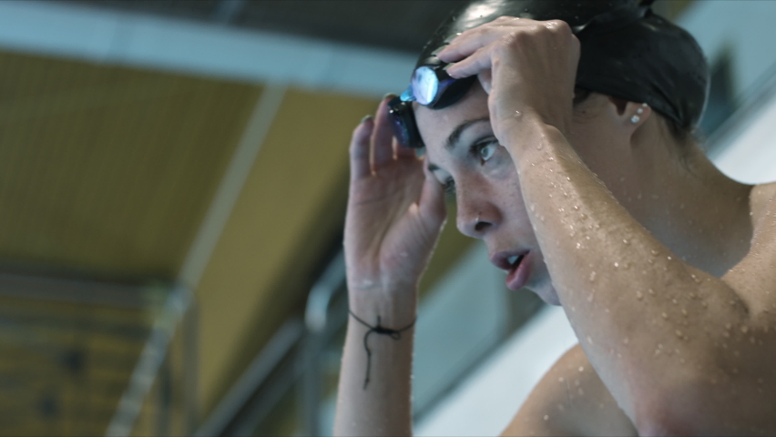 Woman athlete nervously take a deep breath, focus to start swimming, put her goggles on and prepare to jump to the pool. Slow motion video. Top shot. Royalty-Free Stock Footage #1063818445