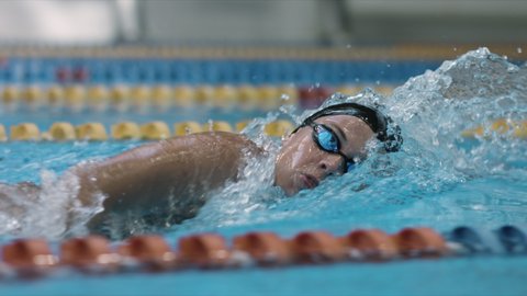 Young female swimmer performing front crawl technique. Sport and endurance theme. Camera moving with woman swimmer.