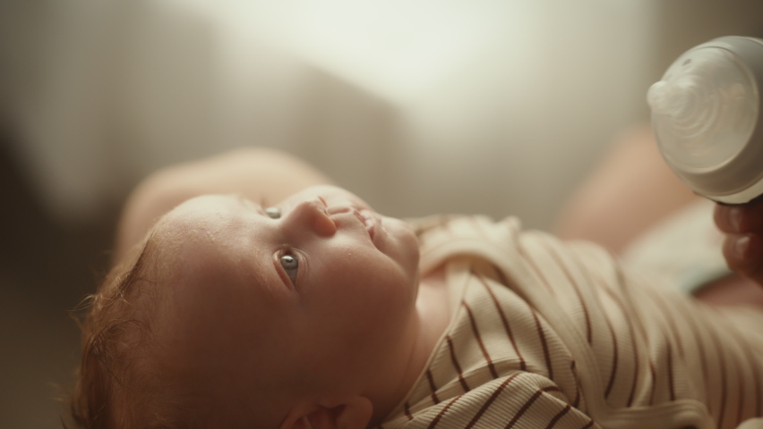 Authentic Close Up Footage of a Newborn Drinking Milk from Small Baby Bottle while Lying on the Back in Child Crib. Portrait of Caucasian Neonate Toddler at Home. Concept of Childhood and Parenthood. Royalty-Free Stock Footage #1063819891