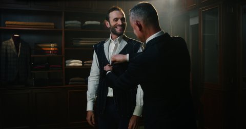 Cinematic shot of professional tailor taking measurements of client for creation custom tailored suit in a luxury tailoring atelier. Concept of fashion, handmade, hand craft, couturier and business
