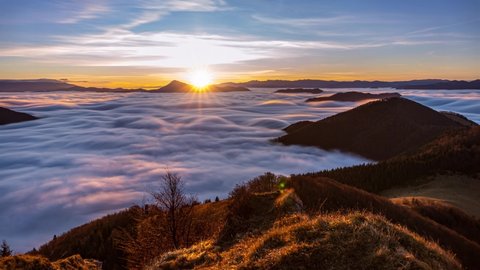 Beautiful light of sunrise sky in wild misty nature with wave of low clouds in alpine mountains valley Time lapse