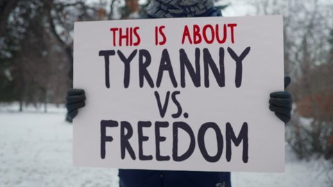 Political protest in a cold winter park. A person is holding up a sign with words This is about Tyranny vs. Freedom. Advocating for human rights. Drawing attention to unjust laws and regulations.