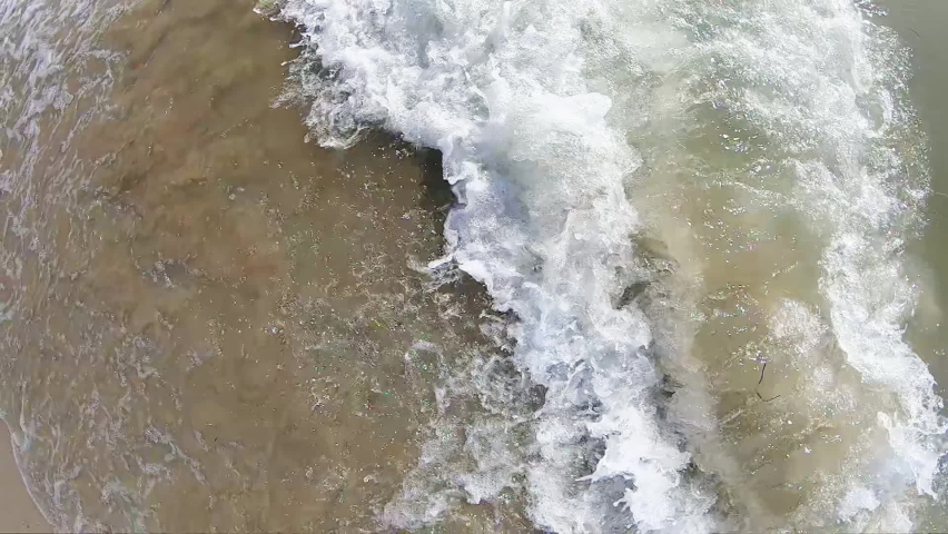 Close up of waves splashing sandy beach, top slow motion view, visible sand noice
