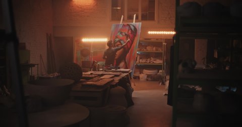 Back view of male artist painting portrait of black woman on easel against lamp during work in spacious workshop