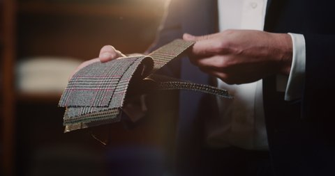 Cinematic shot of young businessman is choosing fabrics for his new custom tailored suit by designer in a luxury tailoring atelier. Concept of fashion, handmade, hand craft, couturier and business.