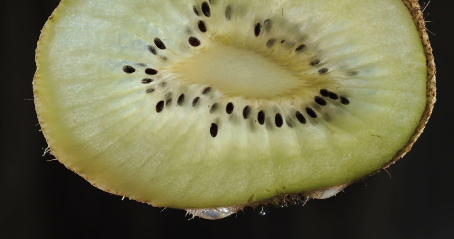 Half a kiwi on a black background with several drops of juice falling