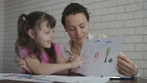 Therapist listen the child. A happy pretty little girl talk about her drawing of family with psychologist in the room.