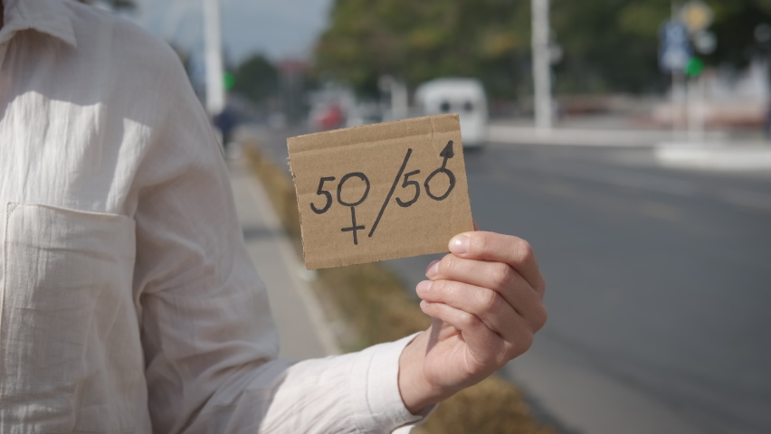 50 to 50. Equality of women. A woman in the city holding a 50-50 sign.