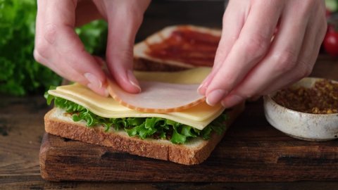 Making a sandwich with ham, cheese, salad and tomatoes. Female chef preparing tasty sandwich