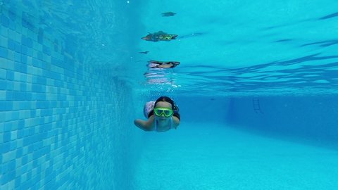 Slow motion view little 7 - 8 years old girl wear swimsuit and goggles submerged in water enjoy summer vacations swimming in pool. Active lifestyle and sport activity concept