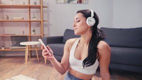 Smiling sportswoman using smartphone and headphones at home