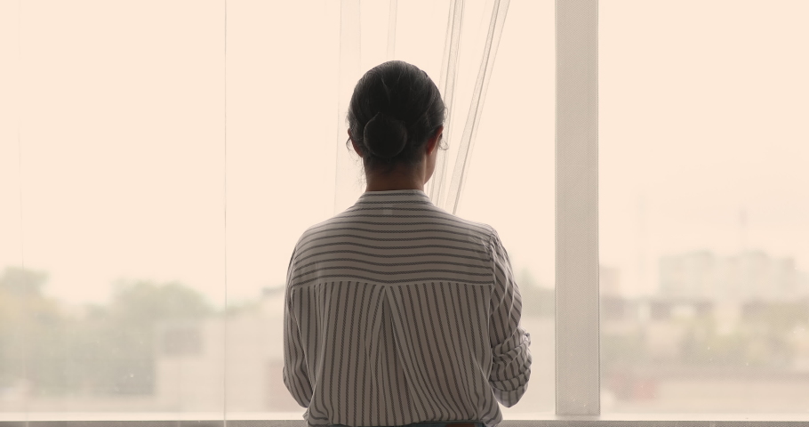 Rear view young woman standing in cozy warm apartment feels carefree and happy opening curtains let light into room, welcoming new day in the morning at home alone. Happy future, aspirations concept Royalty-Free Stock Footage #1063839022