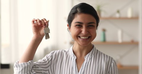 Head shot of Indian female showing keys from new apartment. Happy homeowner portrait, real estate agent selling property. Housing improvement, bank loan and modern house purchase, insurance concept