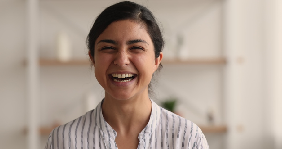 Head shot close up portrait cheerful young Indian female looking very happy, posing indoor. Woman revealing healthy white teeth while laughs over joke, having untroubled mood, pretty face, fun concept Royalty-Free Stock Footage #1063839271