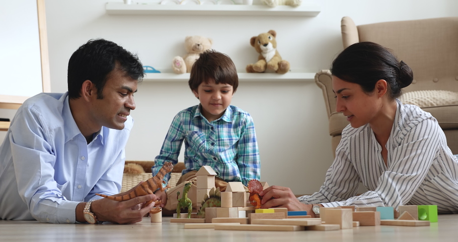 Indian couple and little son play dinosaurs toys and wooden cube set spend time at modern warm comfort home. Kid development, parenthood, playtime and fun with playthings, weekend with family concept Royalty-Free Stock Footage #1063839382