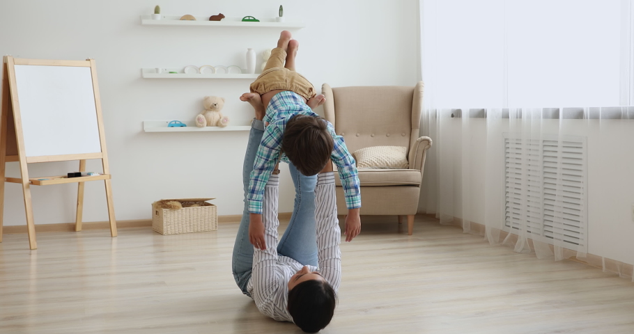 Indian woman play with little son while lying on warm wooden floor in living room lifting up happy kid boy, child looks like fly in air pretends a plane dream together about family travel, fun concept Royalty-Free Stock Footage #1063839433