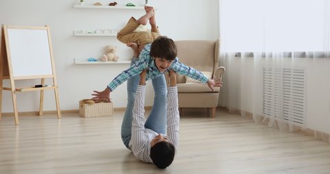 Indian woman play with little son while lying on warm wooden floor in living room lifting up happy kid boy, child looks like fly in air pretends a plane dream together about family travel, fun concept