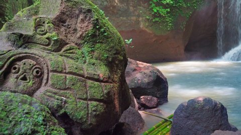 Beautiful waterfall hidden in tropical rainforest jungle with bamboo raft on background scenery stone carving stone in Maya style. 4K Travel in wild nature