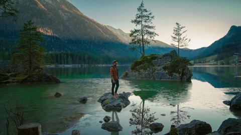 4k UHD Cinemagraph (seamless video loop) of a young man standing on a rock at the scenic travel destination, mountain lake Hintersee in Bavaria, a perfect in Germany with the water moving gently.