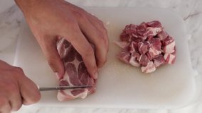 Closeup of a mans hand cutting pork chops on a white board with a steel knife. Home cooking concept.