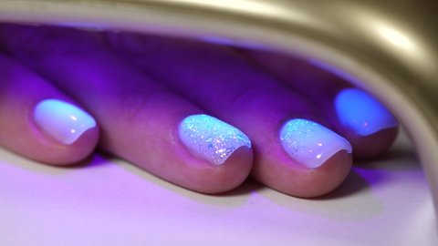 Closeup view 4k video of female blue nails and skin because of blue light of led lamp. Technology for curing and drying nails covered with modern trendy gel polish.