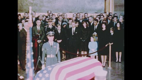 1960s Washington DC: Jackie, Bobby and Caroline Kennedy in crowd near soldier and flag-draped coffin, Jackie holds Caroline's hand, crowd starts to leave